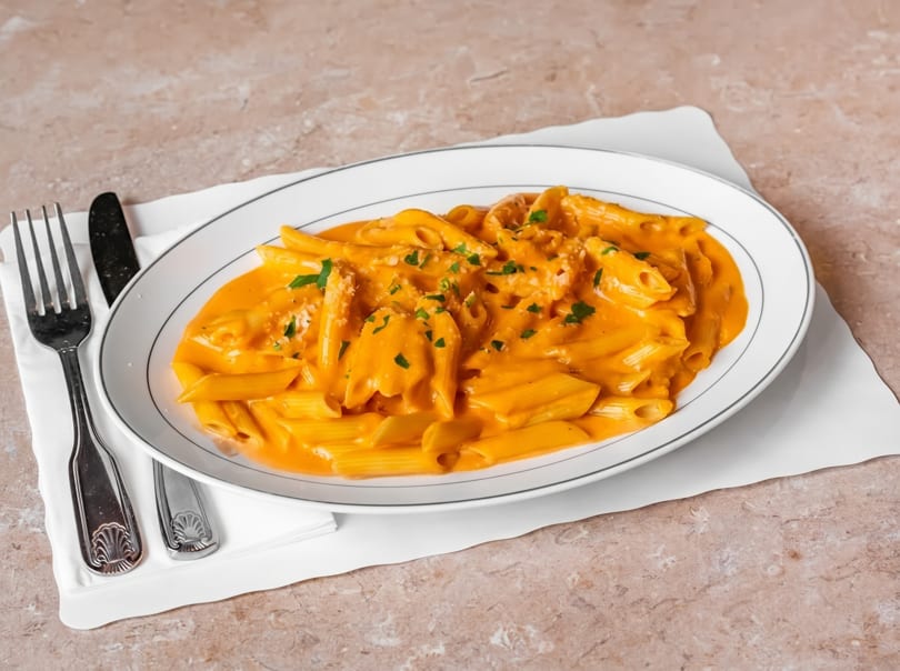 Penne pasta in a creamy orange sauce, garnished with parsley and parmesan cheese.