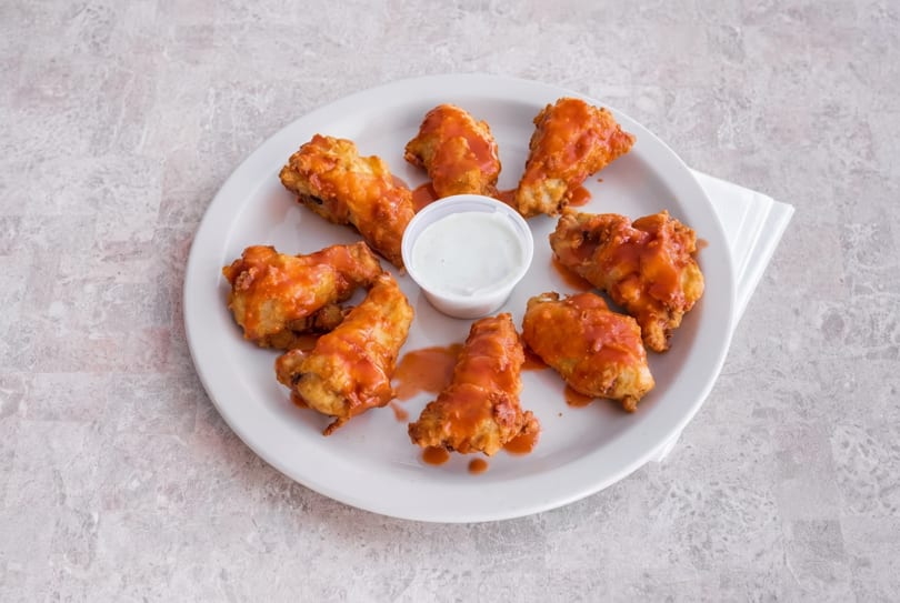 A white plate holds eight buffalo chicken wings with a side of ranch dressing.